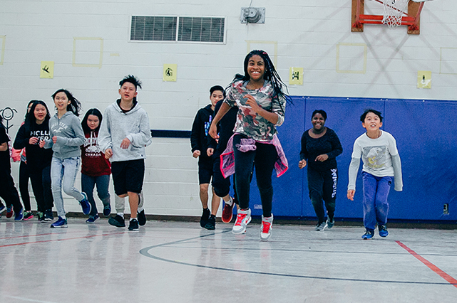 Girl running in gym with classmates running behind her